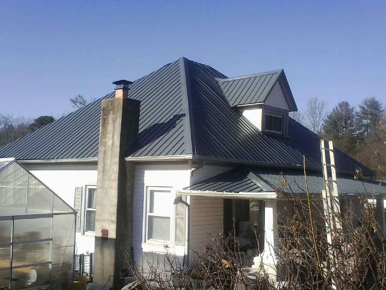 Dark blue standing seam metal roof on a white farmhouse with dormer — Slate & Tile Roof Repair by Roofing Brothers in Sugar Land