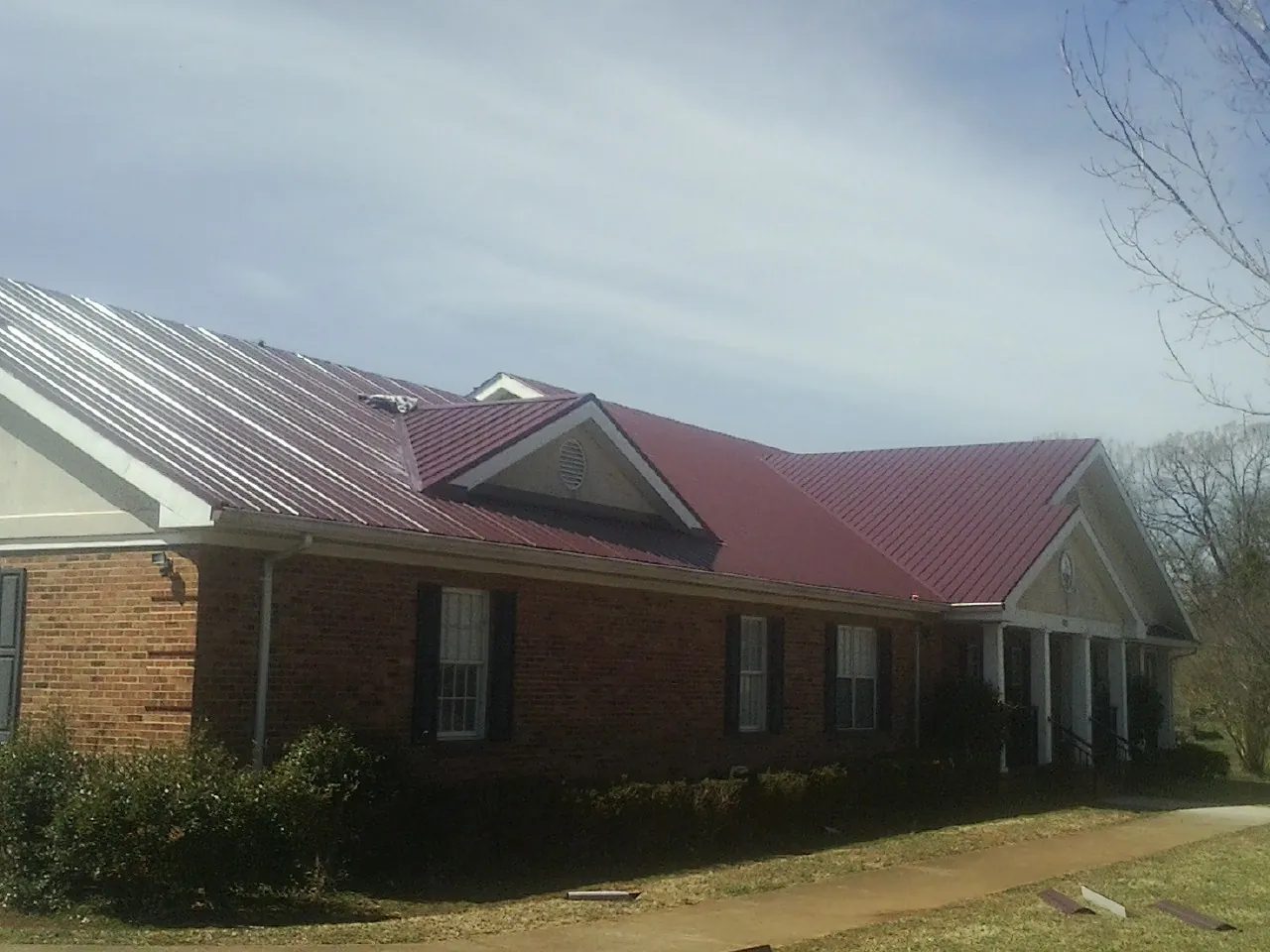 Red metal roof with gabled entries on a long brick building, from a Hail Damage Roof Repair job in Sugar Land
