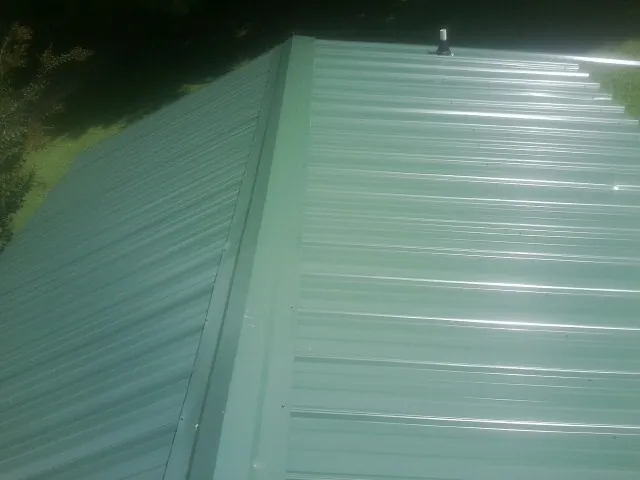 New green metal panels meeting at the ridge of a roof — Flat Roof Repair work by our crew in Sugar Land