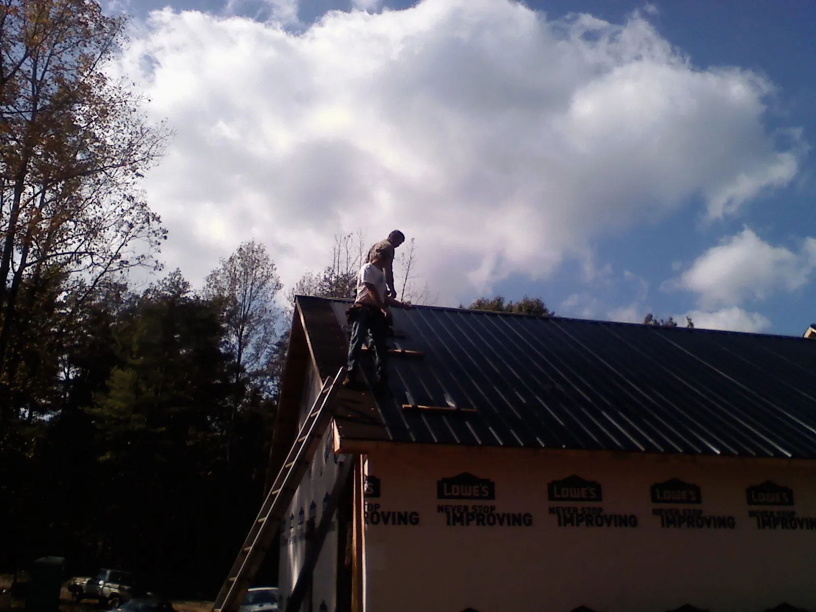Roofer fastening dark metal panels high against a cloudy sky, from a Roof Inspection job in Sugar Land