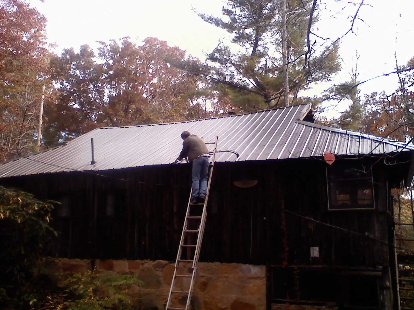 Roofer on a ladder working along the edge of a cabin metal roof in Sugar Land