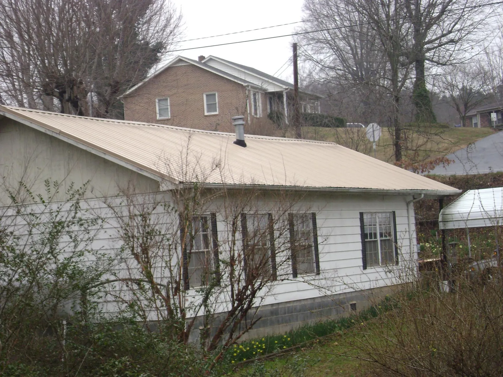 Tan metal roof on a white sided house set into a hillside — Commercial Roofing by Roofing Brothers in Sugar Land