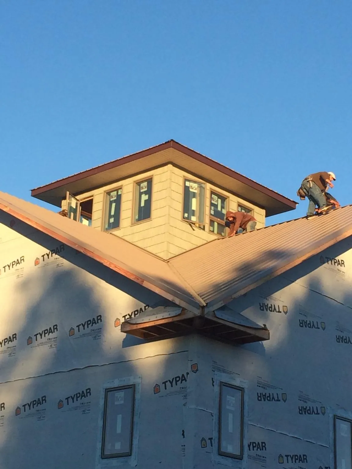 Roofers working around a rooftop cupola on a new metal roof at sunset — Roof Waterproofing in Sugar Land by Roofing Brothers